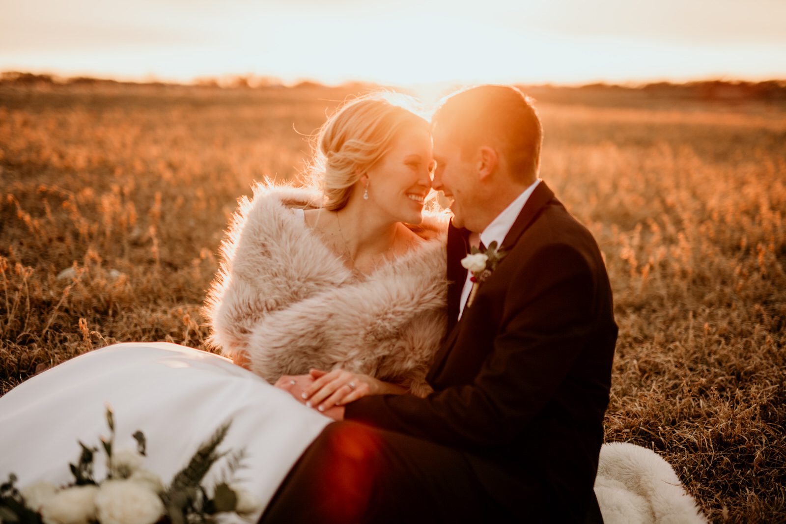 bride and groom nose to nose sitting in a field at golden hour during sunset in rural iowa winter wedding