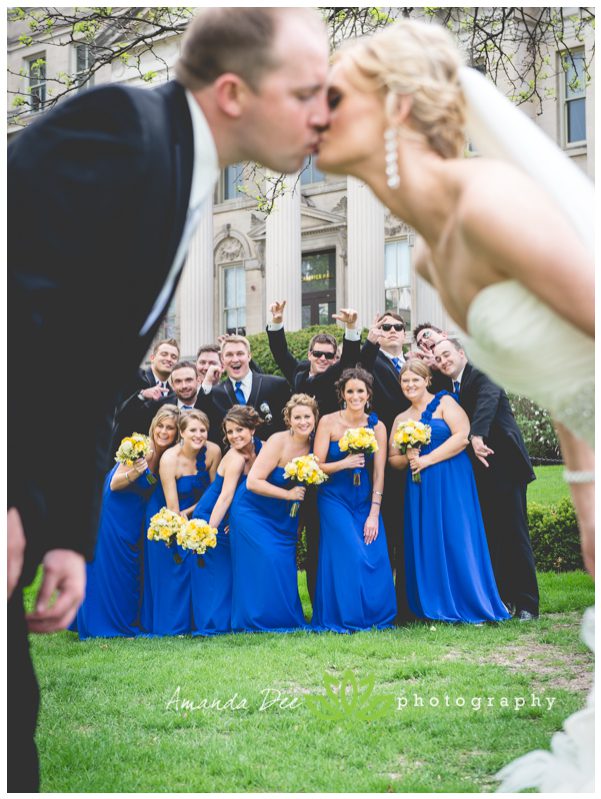 bride and groom kissing with wedding party in background