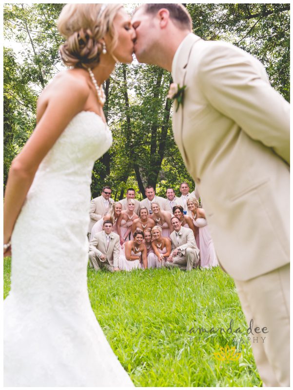 Summer Wedding Amanda Dee Photography bride and groom kissing in foreground bridal party in background